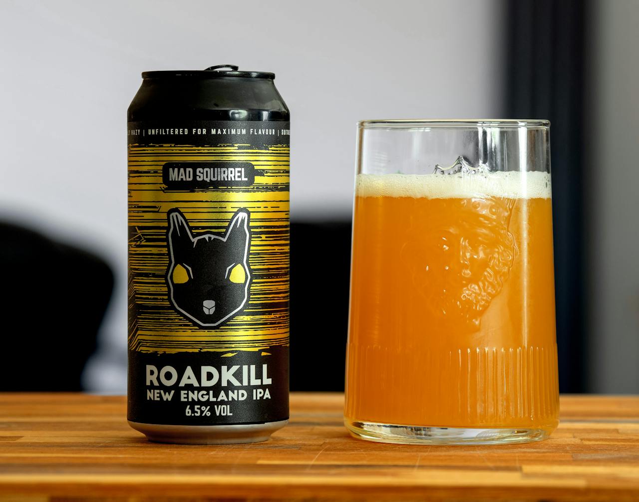 hero-img Close-up of Mad Squirrel Roadkill New England IPA can and full glass on wooden surface.