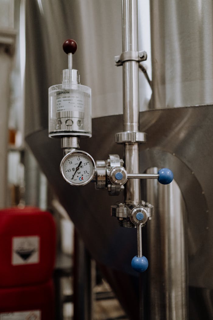Close-up of stainless steel brewery equipment featuring a pressure gauge and control knobs.